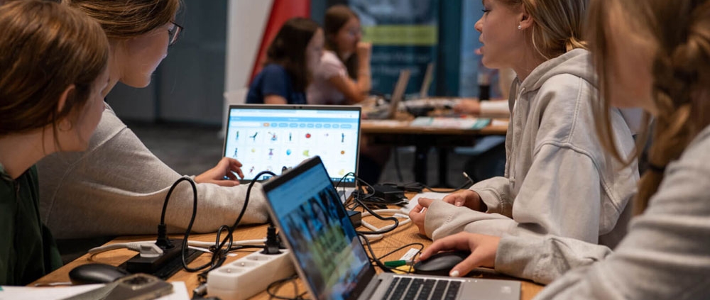 4 Mädchen arbeiten mit 2 Laptops an ihrem Digital Girls Hackathon Projekt