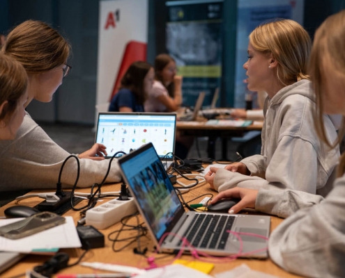 4 Mädchen arbeiten mit 2 Laptops an ihrem Digital Girls Hackathon Projekt