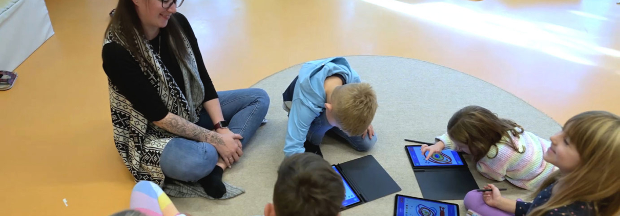 Kindergarten-Pädagogin und Kinder mit iPads sitzen auf Boden