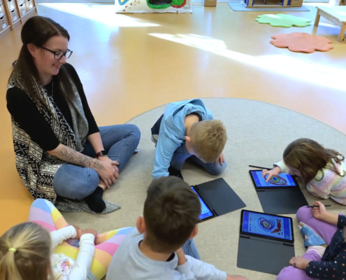 Kindergarten-Pädagogin und Kinder mit iPads sitzen auf Boden