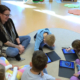 Kindergarten-Pädagogin und Kinder mit iPads sitzen auf Boden