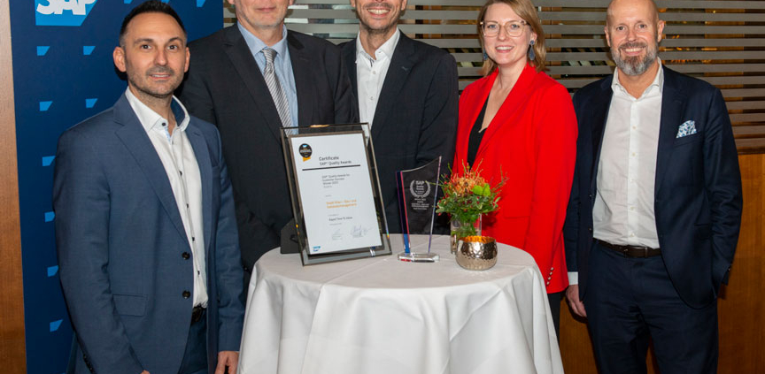 5 Personen stehen hinter Tisch mit Urkunde und Award