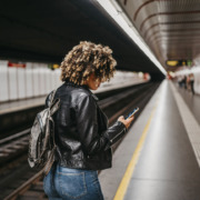 Frau steht an einer U-Bahn-Haltestelle und schaut auf ihr Smartphone