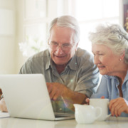 2 Senior*innen arbeiten am Laptop. Beide haben eine Tasse bei sich stehen.