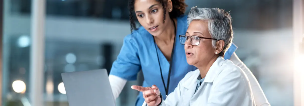 2 Ärztinnen sehen auf einen Laptop-Bildschirm und besprechen etwas.