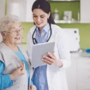 Ärztin und ältere Patientin blicken auf ein Tablet.