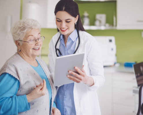 Ärztin und ältere Patientin blicken auf ein Tablet.