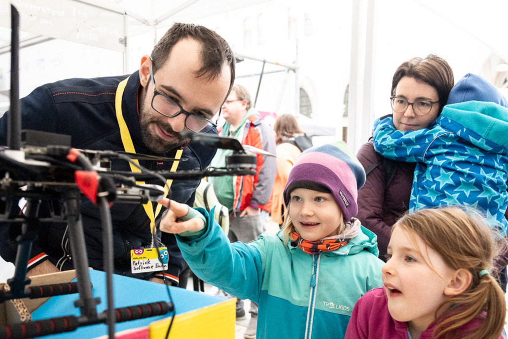 Kinder und Erwachsene betrachten eine Drohne.