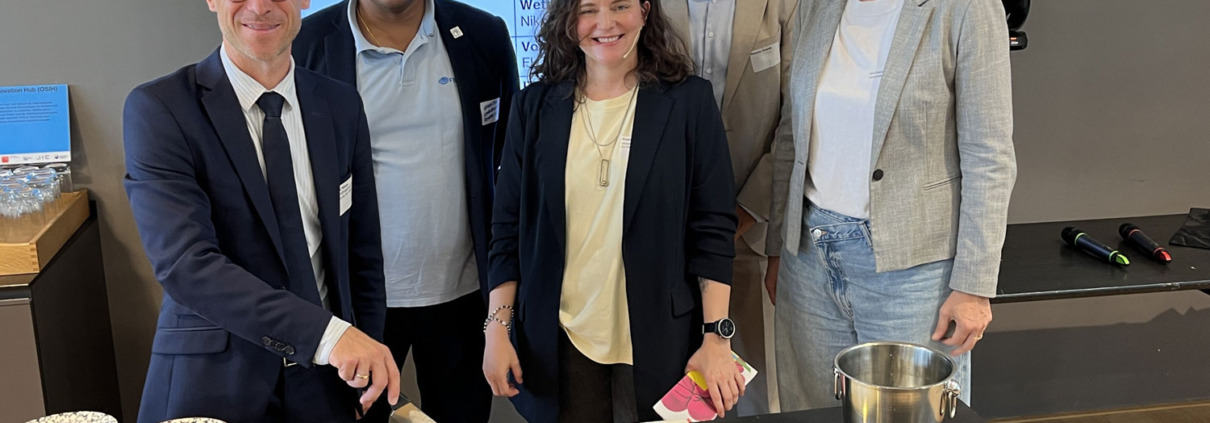 3 Männer, 2 Frauen, ein Mann schneidet einen Kuchen an