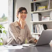 Eine Junge Frau sitzt lächelnd vor einem Laptop in einem Büro.