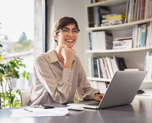 Eine Junge Frau sitzt lächelnd vor einem Laptop in einem Büro.