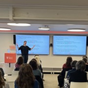 Vortragende, im Publikum Frauen, im Hintergrund elektronische Tafeln