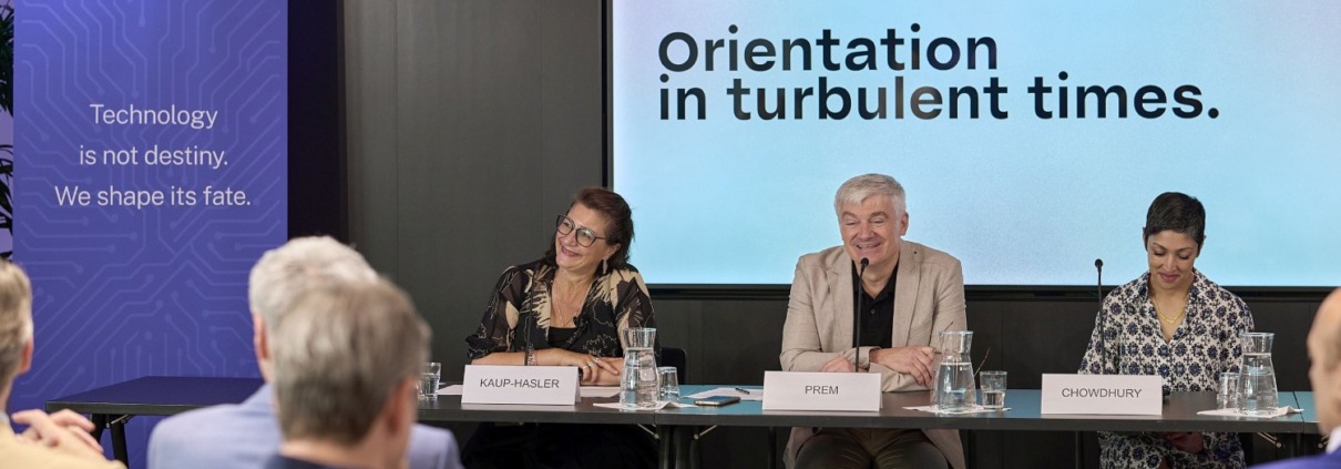 2 Frauen, ein Mann an Tischen bei einer Konferenz