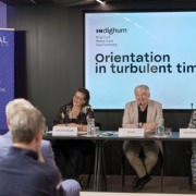 2 Frauen, ein Mann an Tischen bei einer Konferenz
