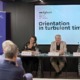 2 Frauen, ein Mann an Tischen bei einer Konferenz